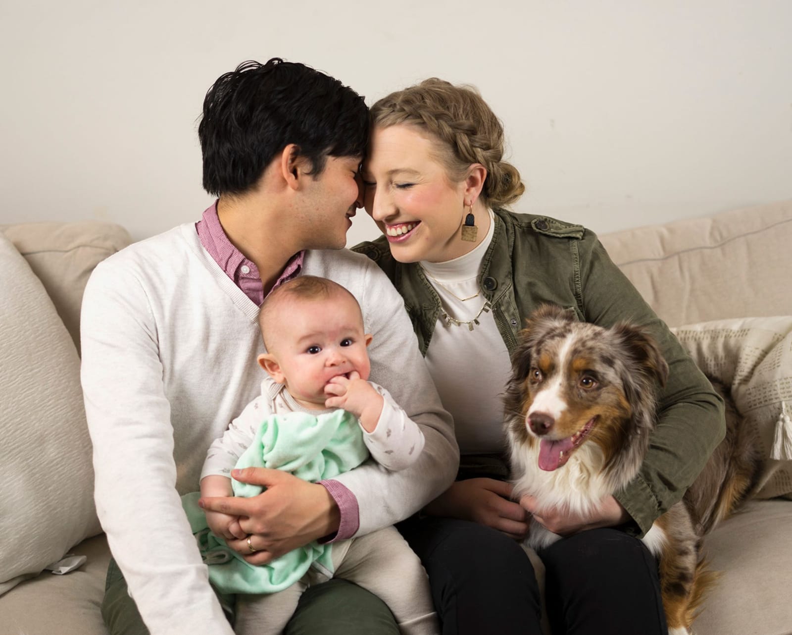 Two parents and their dog cuddled around their baby on a couch