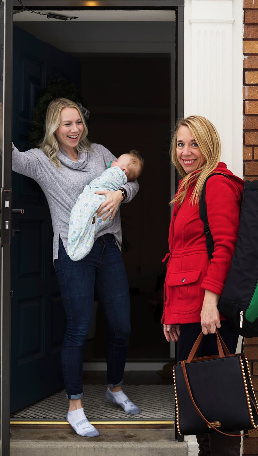 Julie arriving at a family's front door with her visit bag, greeted by a mother holding her newborn