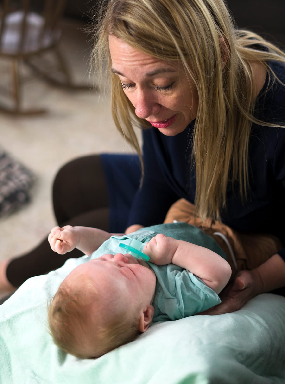 Julie bending over a newborn lying on a mint blanket, her hands resting lightly on the baby