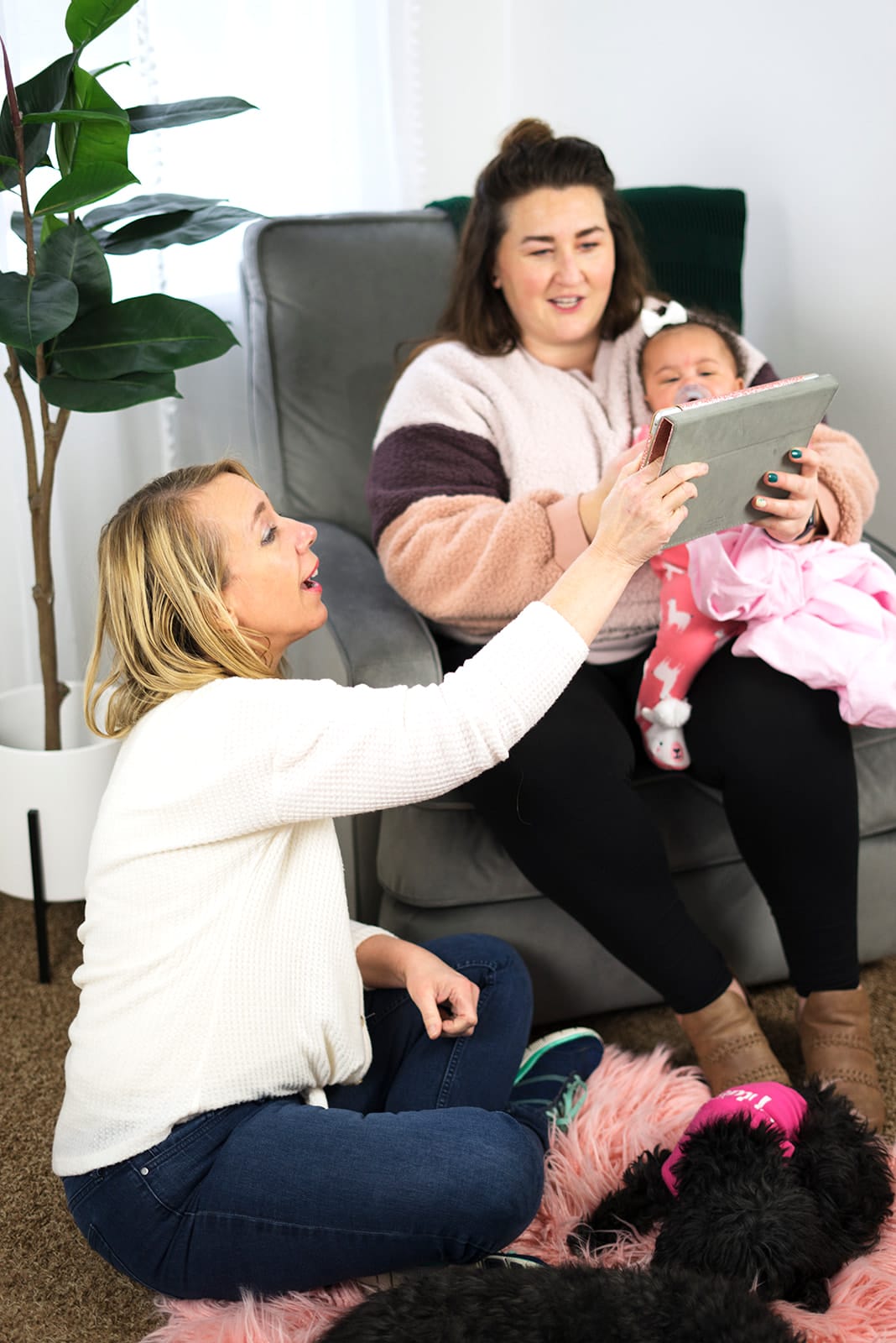 Julie kneeling on the floor beside a mother who is sitting in an armchair with her baby