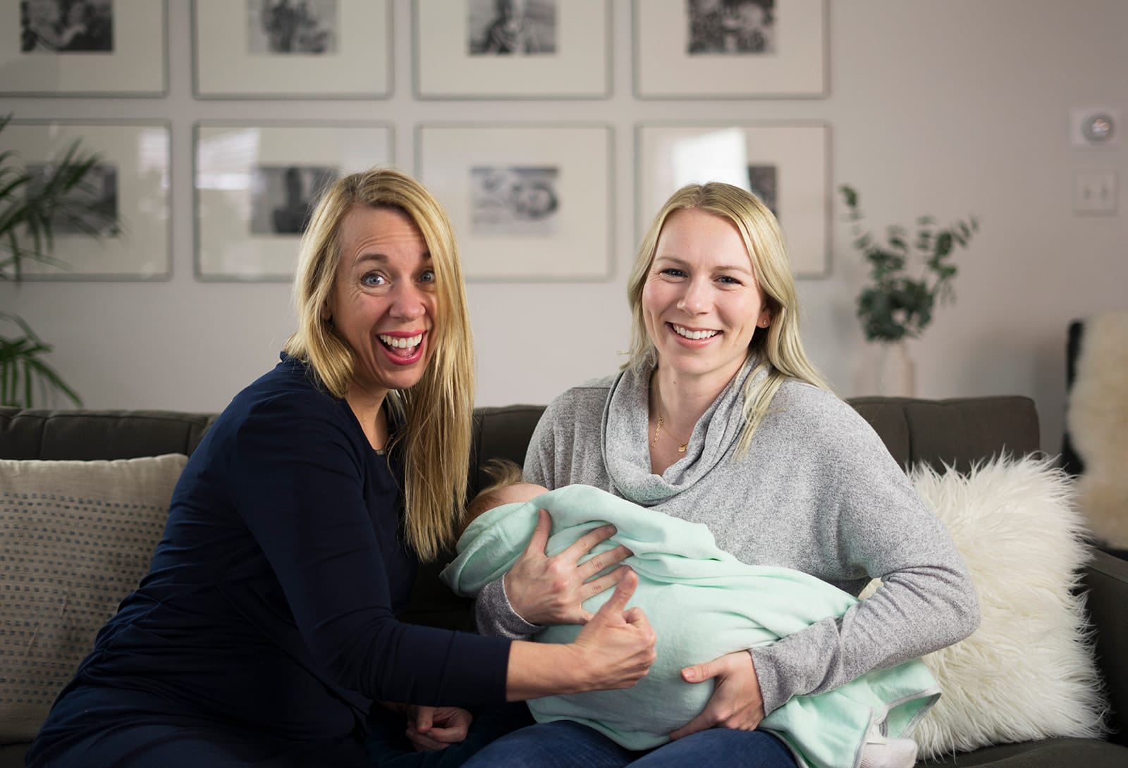 Julie and a mother sitting close together on a couch, the mother holding her swaddled baby